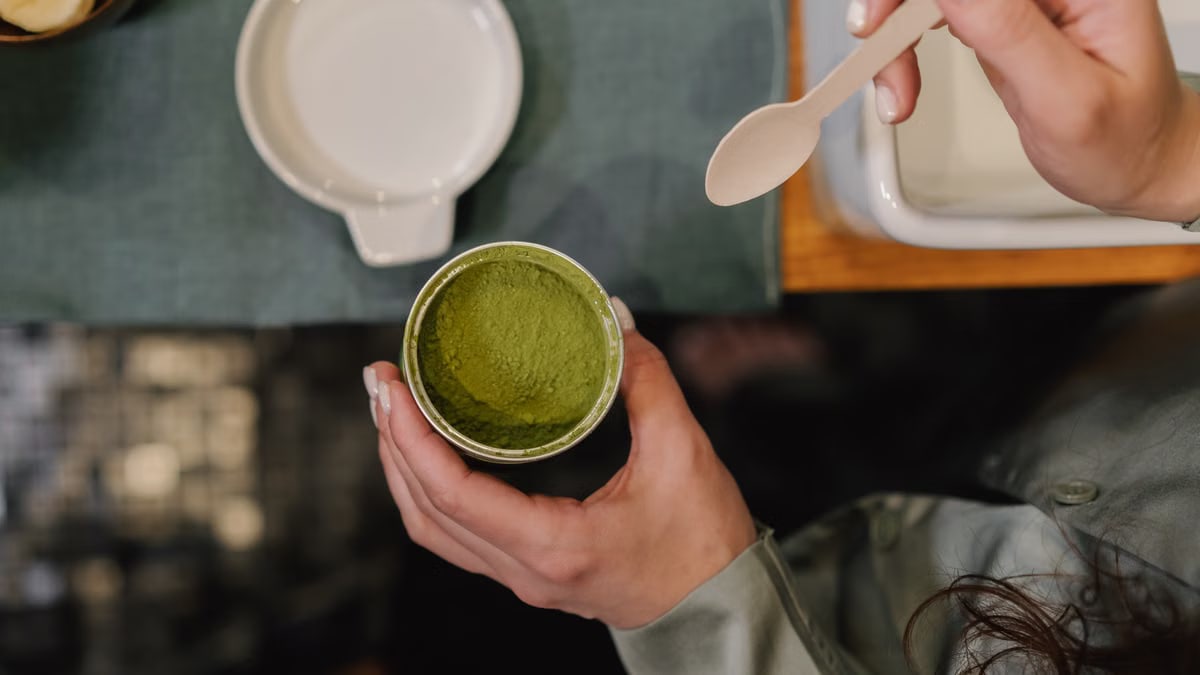 A person holding a container of matcha powder with a spoon, ready for use.